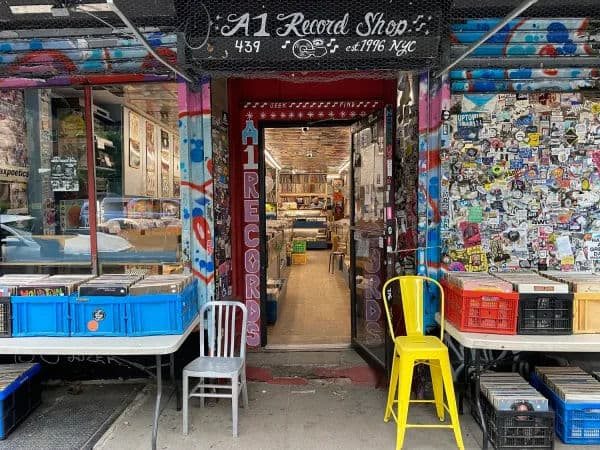 Exterior of A1 Record Shop in New York City, with a colorful graffiti-covered storefront, sticker-covered wall, and open doorway leading into rows of vinyl inside.