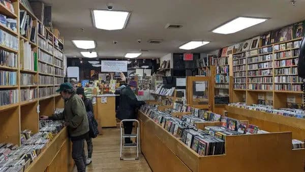 Interior of Academy Records & CDs, with tall wooden shelves stacked with CDs and vinyl. Several customers browse the aisles.