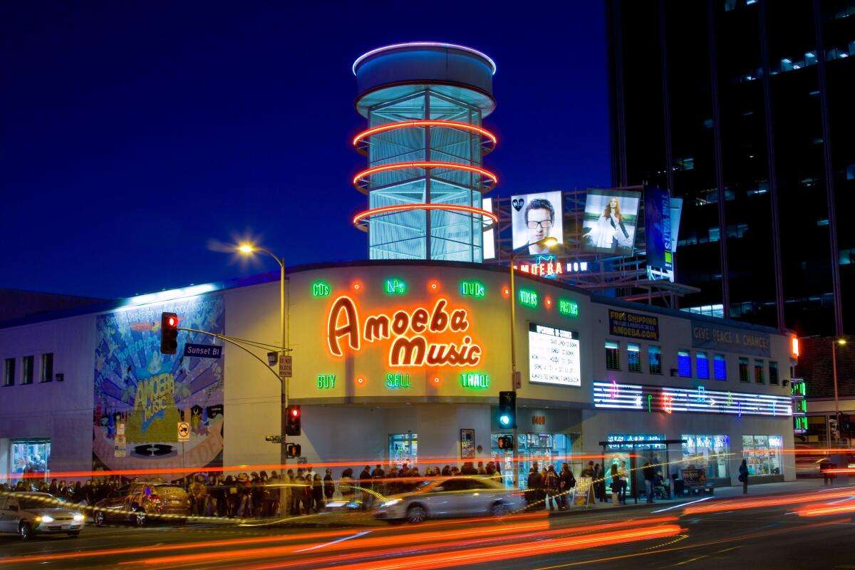 Night view of Amoeba Music in Los Angeles, glowing with neon red and green lights as cars pass by on Sunset Boulevard.
