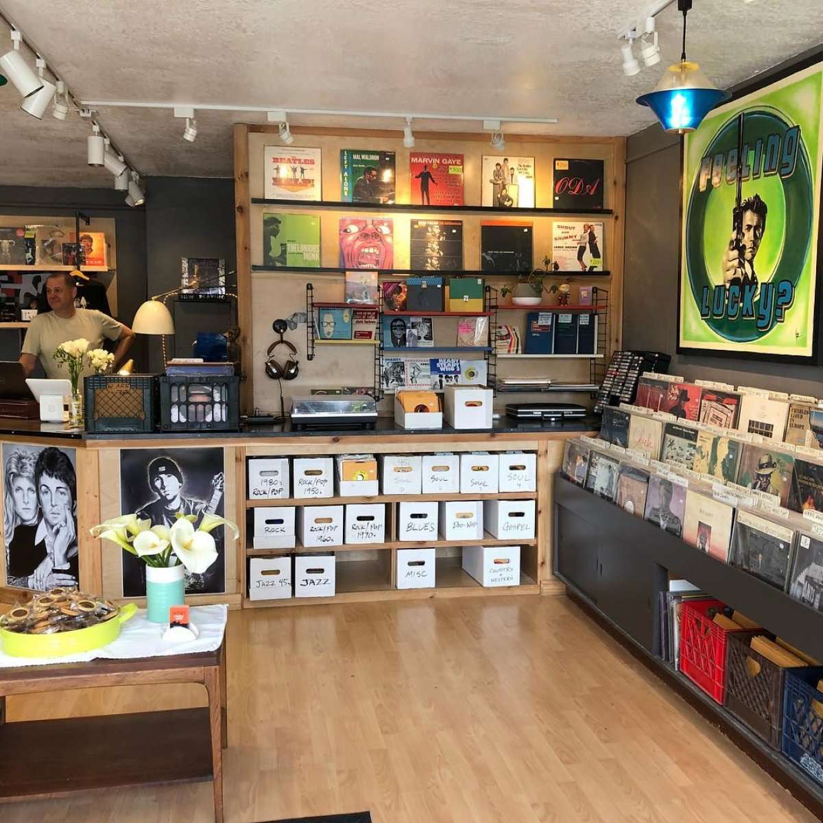 Cozy Berkeley record store interior with wall of LPs, genre crates, and a Feeling Lucky? poster.