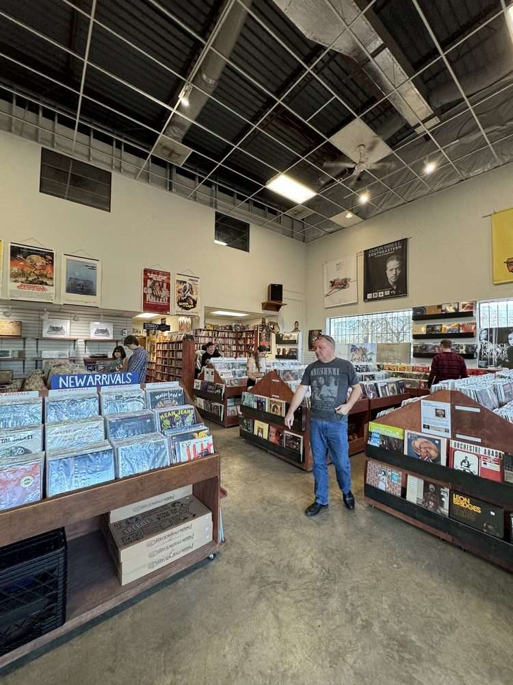 Spacious record store interior with high ceilings, hanging posters, and rows of wooden bins filled with vinyl records.