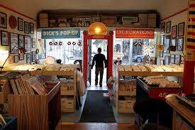Cozy vintage record shop in SF packed with 45s and LP bins, framed posters on the walls, and an open front door to the street.