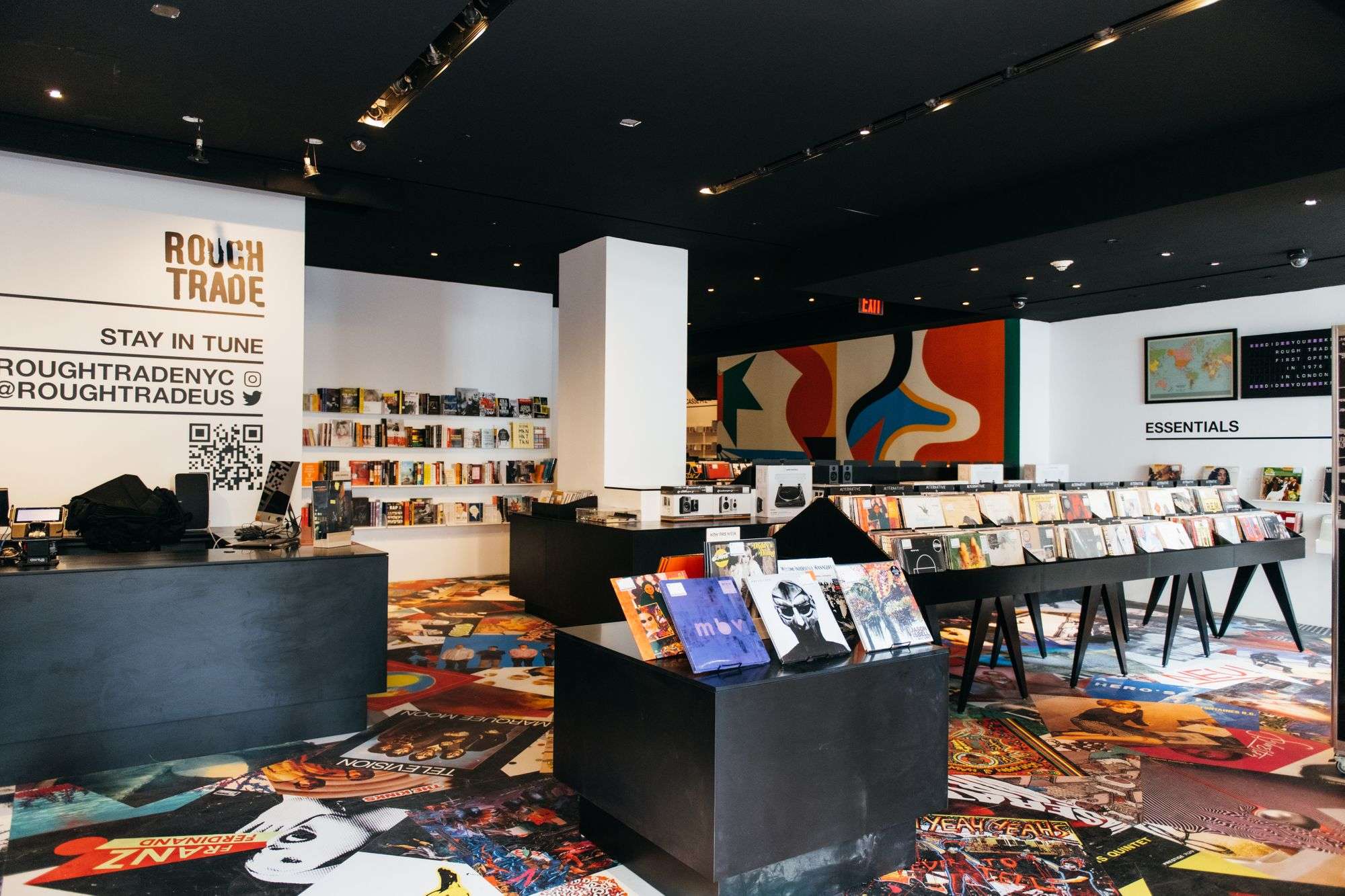 Interior of Rough Trade record store in New York City, featuring sleek black display tables filled with vinyl records, colorful wall art in the background.