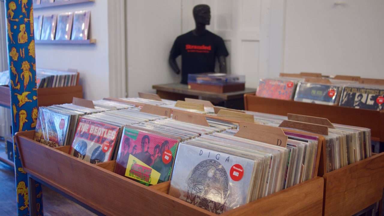 Interior of Stranded Records San Francisco with wooden LP bins, alphabet dividers, wall shelves, and a mannequin in a Stranded shirt.