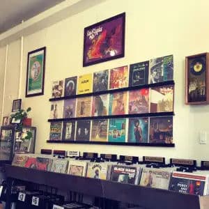 East Bay record shop with wall ledge of LPs, discount $3/$5 bins, and soundtrack/rock sections.