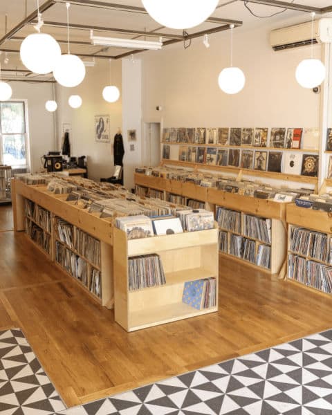 Bright, minimalist record store interior with wooden bins filled with vinyl records and album covers displayed along the back wall.