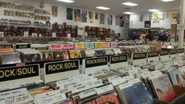 Interior of The Great Escape record store with aisles of vinyl and signs for genres like rock, soul, reggae, and hip hop, with walls lined with posters.