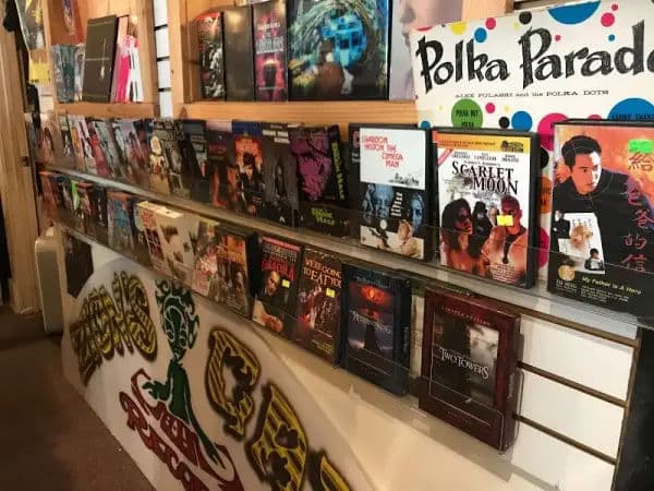 Counter and wall display packed with cult DVDs and vinyl sleeves inside Zion's Gate, with hand-painted shop graphics.